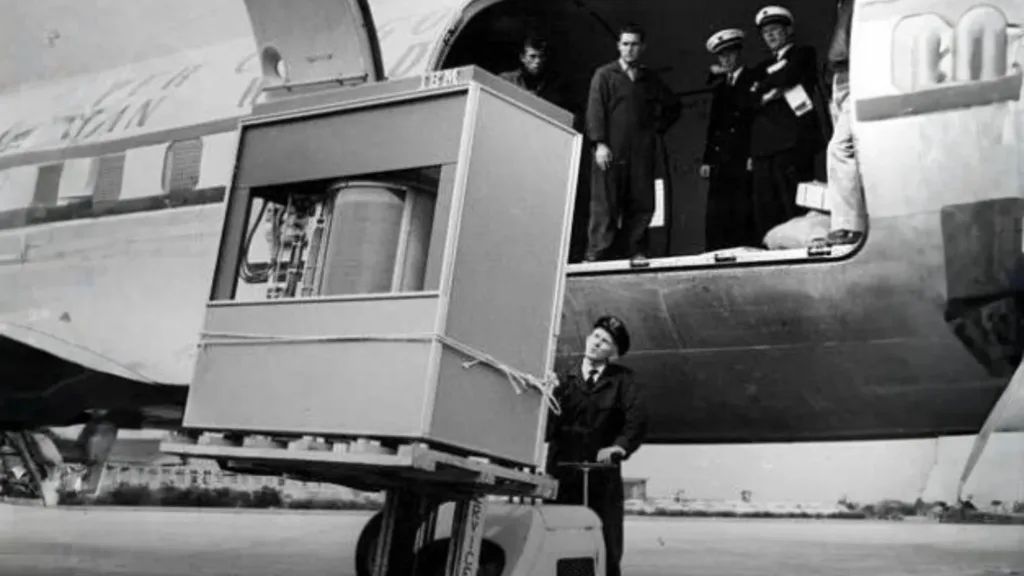 Black and white image of a person loading a 5 megabyte hard drive onto a plane