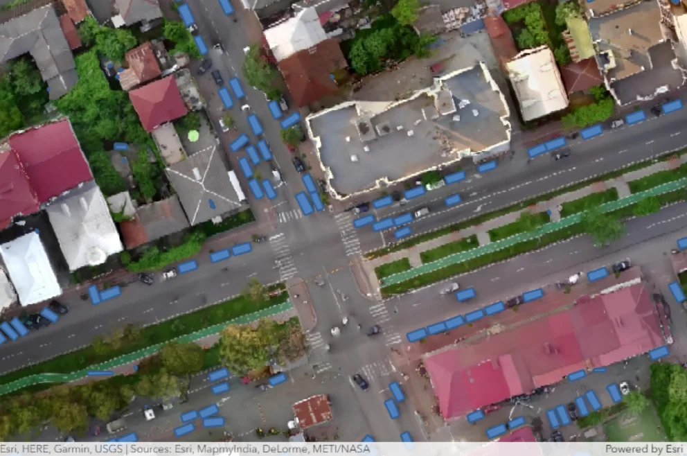 Aerial view of a bustling city street filled with cars and lined with various buildings under a clear blue sky.