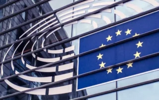 Glass facade of a building displays the European Union flag, with 12 golden stars in a circle on a blue background.