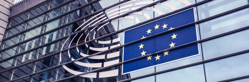 Glass facade of a building displays the European Union flag, with 12 golden stars in a circle on a blue background.